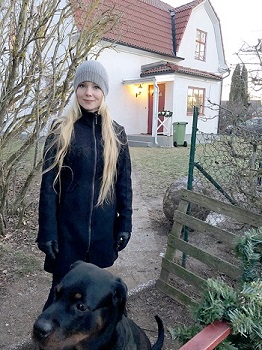 Bild på blond kvinna och svart hund framför ett vitt hus