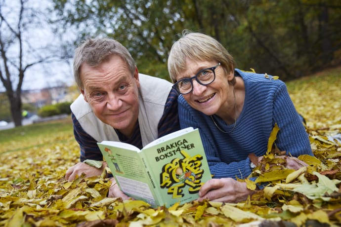 Bild på Illustratören Mati Lepp och författaren Helena Bross, bilden är tagen utomhus och båda två ligger på marken bland löv, Helena håller en bok framför sig