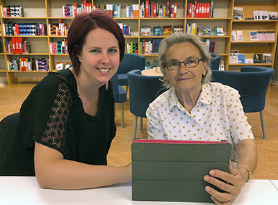 Bild på Emelie Ekholm, kvinna med kort, mörkt hår, som hjälper Gunilla Kvissberg, äldre kvinna med glasögon och vit blus, med sin iPad