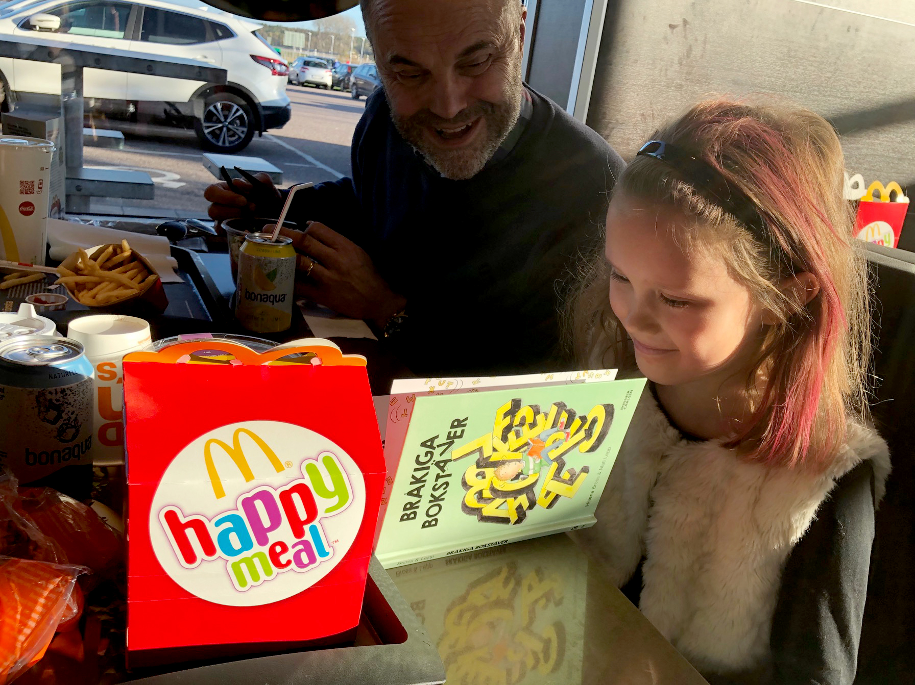 Bild på en tjej som sitter och läser boken Bråkiga bokstäver, bredvid henne står det en Happy Meal-låda.