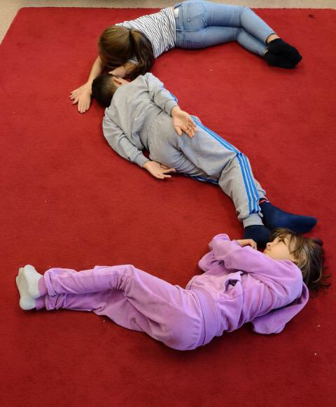 Bild av ett s, i form av tre stycken barn som ligger på golvet.