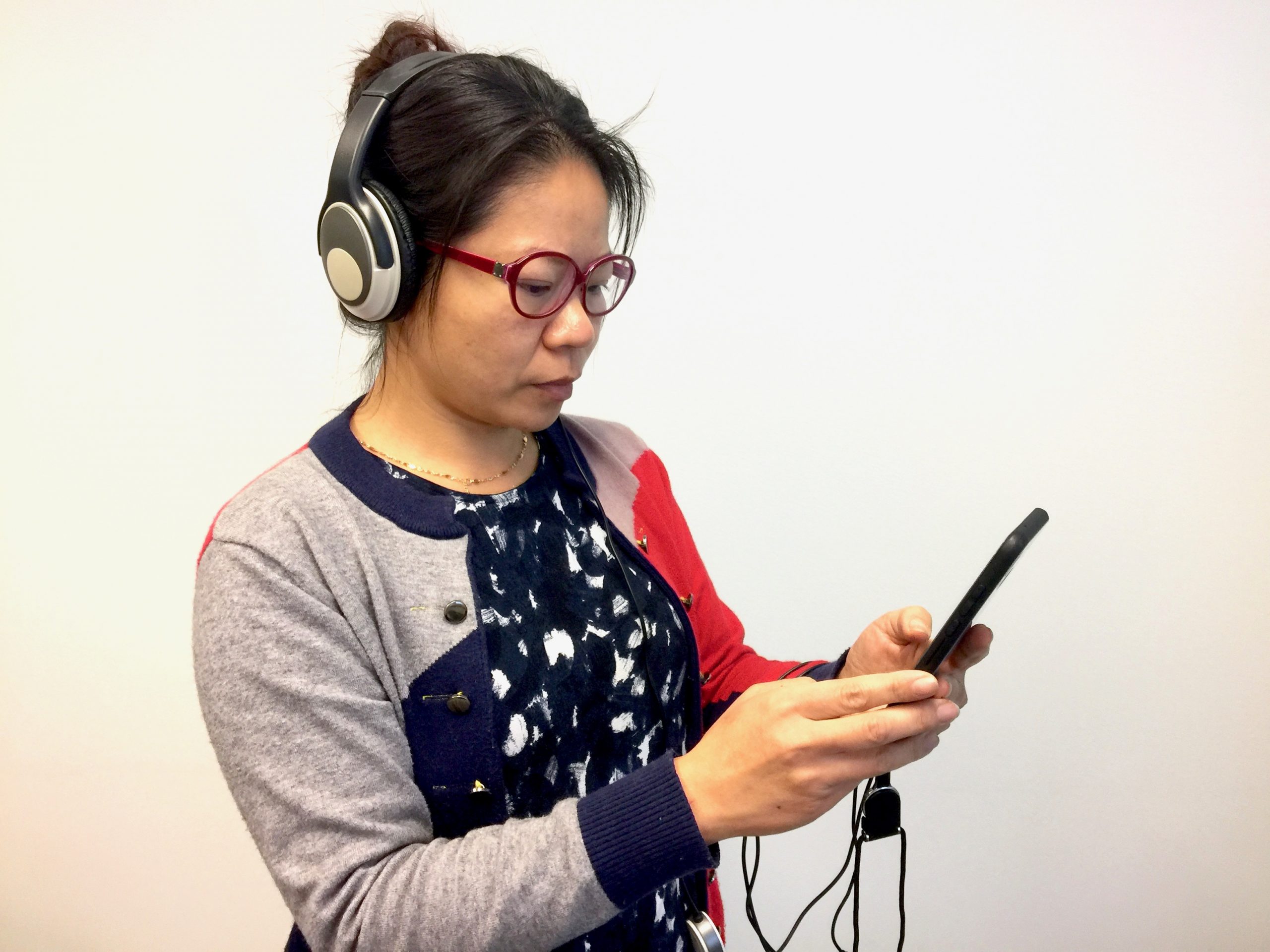Kvinna med hörlurar. Hon lyssnar på talsyntes i mobilen.