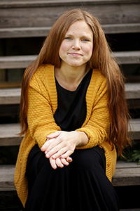 Bild på Terese Raymond, kvinna med lång hår och gul kofta som sitter i en trappa.