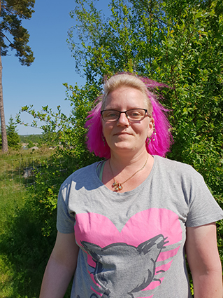 Bild på Kicci Lönnerdahl, kvinna med glasögon och kort, rosa hår iklädd en grå t-shirt.