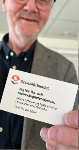 Person visar kort med text: Jag har läs- och skrivsvårigheter/dyslexi